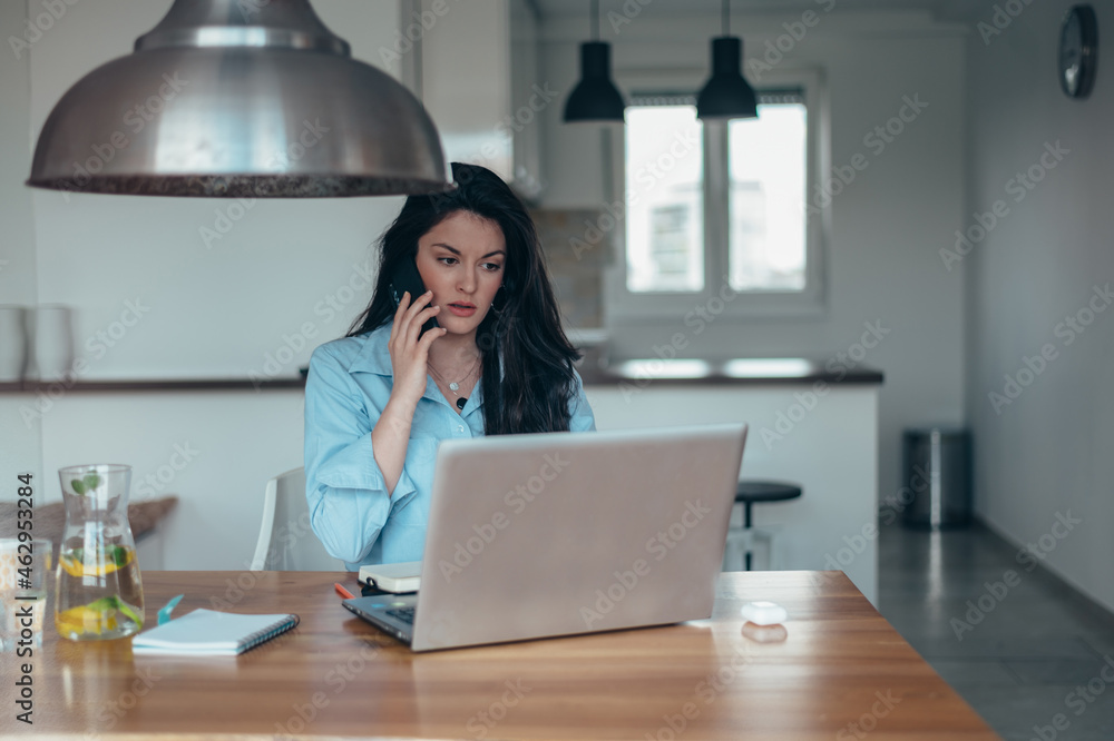Businesswoman using a laptop and a smartphone while working from home Businesswoman using a laptop and a smartphone while working from home