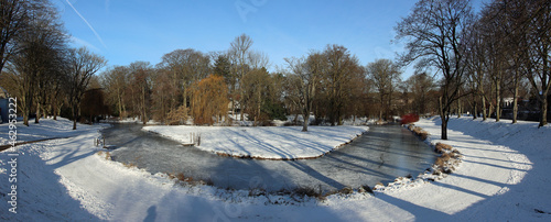 Park of the city of Moers in Germany with an icy brook and snow-covered paths with idyllic blue skies in winter  photo