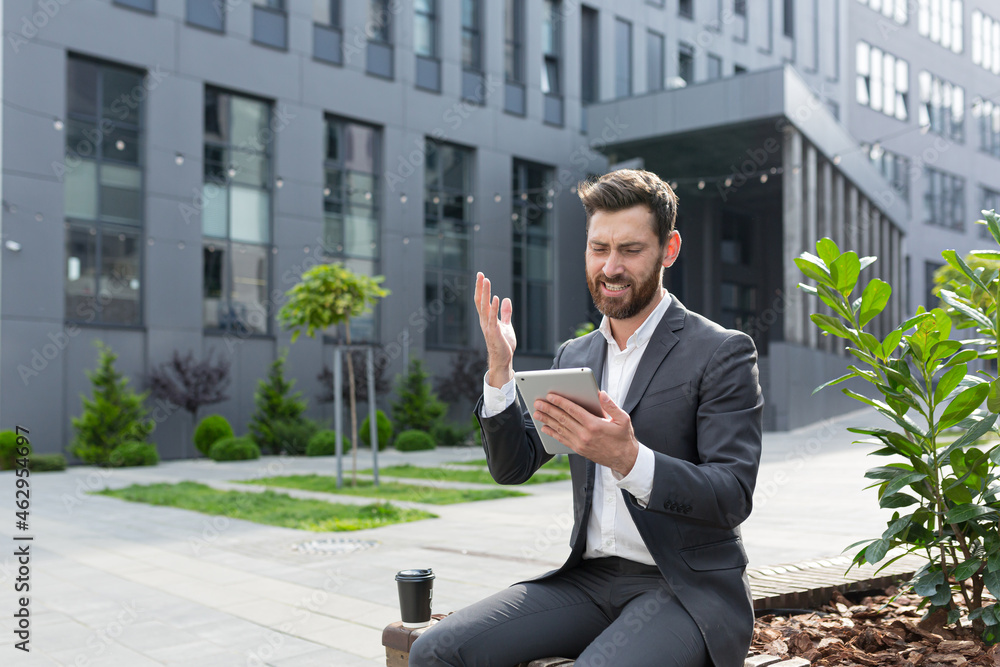 Successful salesman entrepreneur rejoices at a successful deal, receives confirmation of sale online, rejoices sitting near the office holding a tablet Successful salesman entrepreneur rejoices at a successful deal, receives confirmation of sale online, rejoices sitting near the office holding a tablet