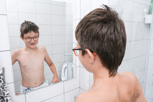 A teen boy looking in a mirror in bathroom and showing muscules photo
