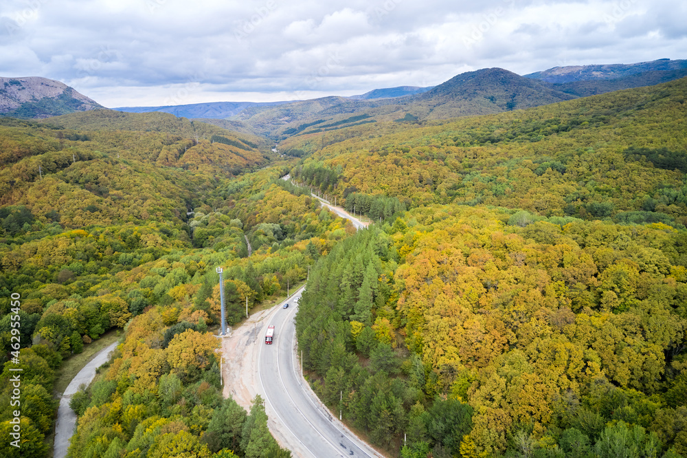 Autumn. A mountainous area with a winding road along which cars are moving. Shooting from a drone.