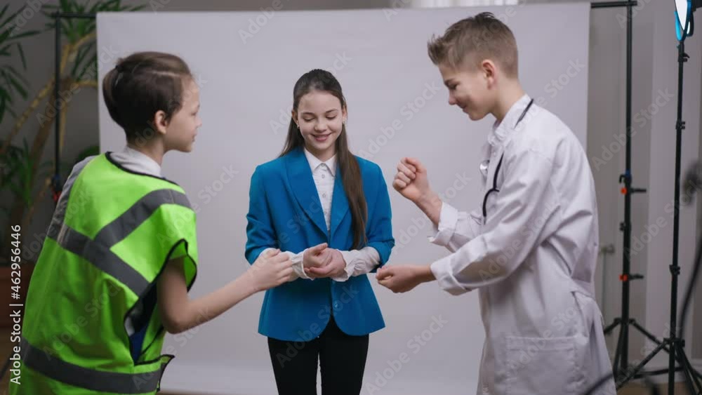Three cheerful carefree teenage boys and girl playing rock paper scissors smiling having fun. Positive joyful Caucasian teenagers in professions uniforms enjoying leisure together indoors. Lifestyle Three cheerful carefree teenage boys and girl playing rock paper scissors smiling having fun. Positive joyful Caucasian teenagers in professions uniforms enjoying leisure together indoors. Lifestyle
