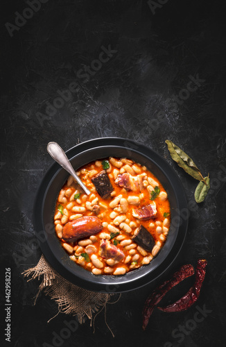 Traditional recipe of beans with chorizo and blood sausage called “Fabada Asturiana” on a dark table with some ingredients around. Typical Spanish food with “compango”. 