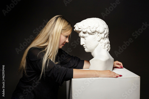 attractive blonde posing with a bust of David. photo shoot in the studio on a black background