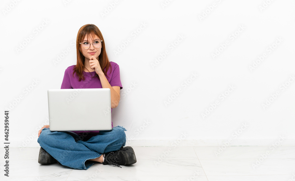 Fototapeta premium redhead girl with a laptop sitting on the floor and looking up