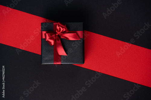 Gift box wrapped in black paper with a red ribbon and bow on a black-red background.