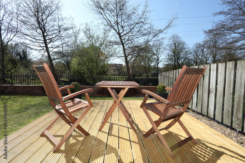two chairs and a table on wooden decking in the garden on a bright and sunny summers day.