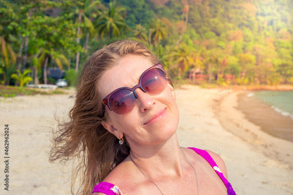 Mature woman with blond hair in sunglasses smiles on a background of palm trees on a tropical island. Mature woman with blond hair in sunglasses smiles on a background of palm trees on a tropical island.