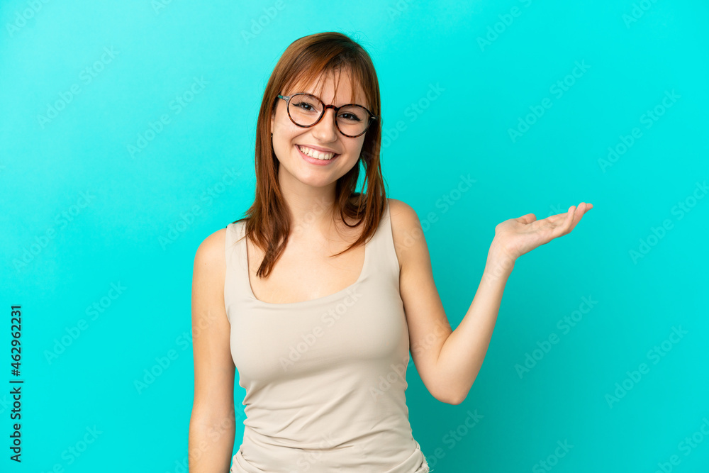 Fototapeta premium Redhead girl isolated on blue background holding copyspace imaginary on the palm to insert an ad