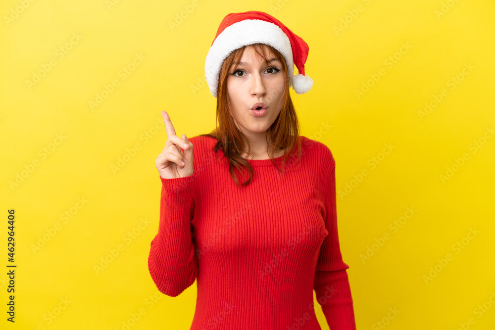 Redhead girl with christmas hat isolated on yellow background intending to realizes the solution while lifting a finger up Redhead girl with christmas hat isolated on yellow background intending to realizes the solution while lifting a finger up