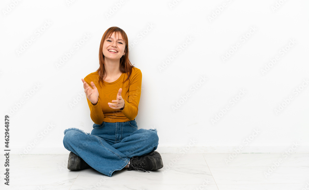 Redhead girl sitting on the floor isolated on white background applauding after presentation in a conference Redhead girl sitting on the floor isolated on white background applauding after presentation in a conference