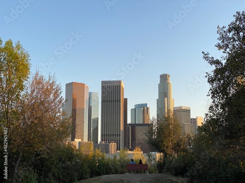 LOS ANGELES, CA, JAN 2021: Downtown skyline with skyscrapers seen from park to the north of the city, people silhouetted on bench in foreground © vesperstock