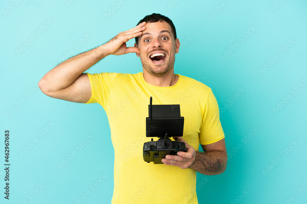 Brazilian man holding a drone remote control over isolated blue background with surprise expression Brazilian man holding a drone remote control over isolated blue background with surprise expression