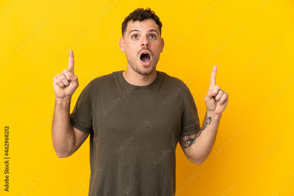 Young caucasian handsome man isolated on yellow background surprised and pointing up Young caucasian handsome man isolated on yellow background surprised and pointing up