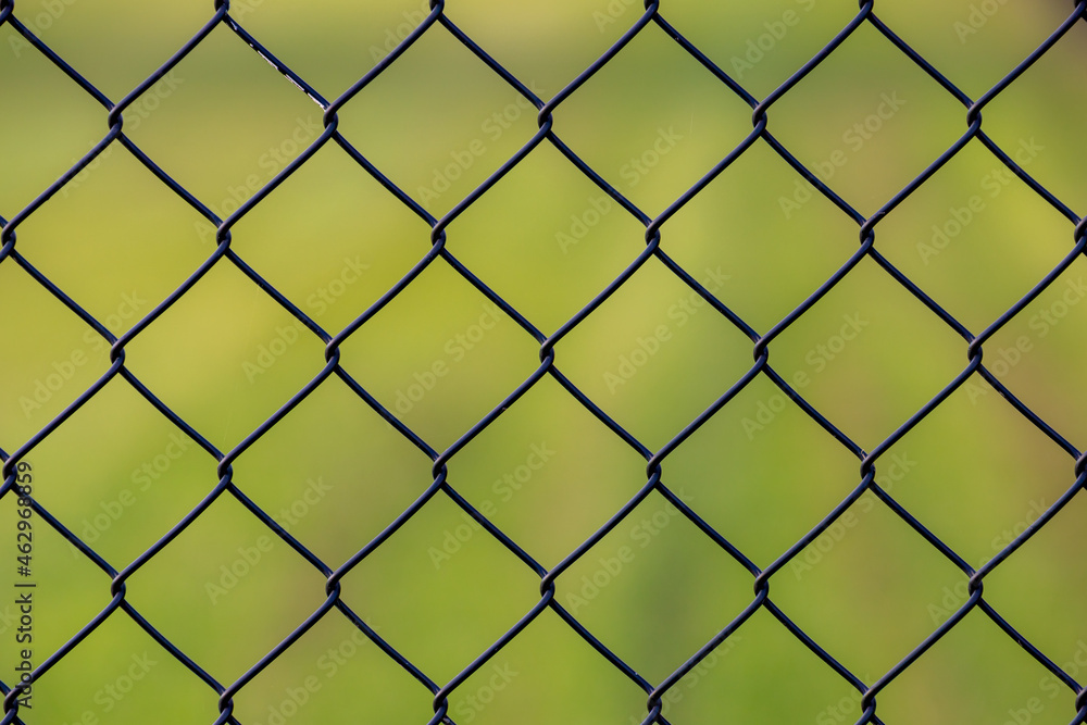 Abstract background, Old metal fence with wire mesh, Steel iron mesh net cage in the garden with green grass as backdrop. Abstract background, Old metal fence with wire mesh, Steel iron mesh net cage in the garden with green grass as backdrop.