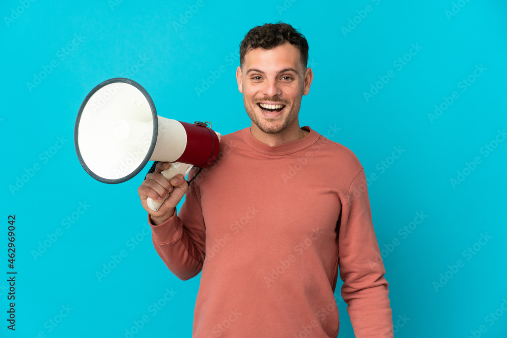 Young caucasian handsome man isolated on blue background holding a megaphone and with surprise expression Young caucasian handsome man isolated on blue background holding a megaphone and with surprise expression