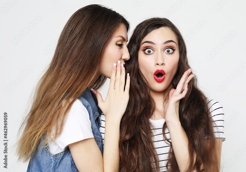 Portrait of two happy young women sharing secrets isolated over white background Portrait of two happy young women sharing secrets isolated over white background