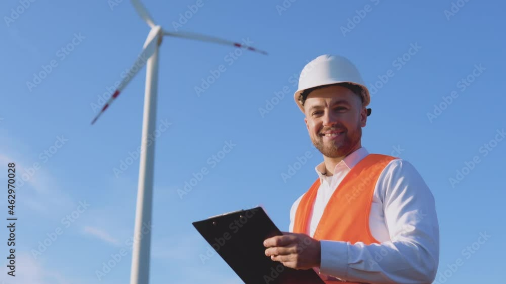 A male engineer in a white helmet, a classic shirt and an orange work vest inspects the power plant's facilities and makes entries in working documents A male engineer in a white helmet, a classic shirt and an orange work vest inspects the power plant's facilities and makes entries in working documents