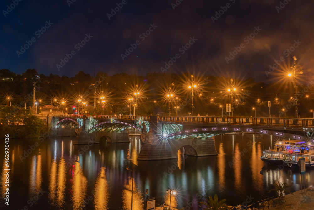 Bridge across Vltava River illuminated at night  with lighting reflected in water
