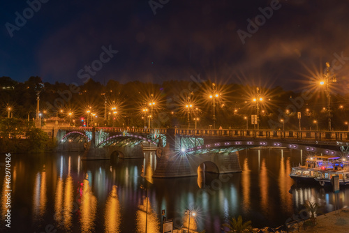 Bridge across Vltava River illuminated at night with lighting reflected in water