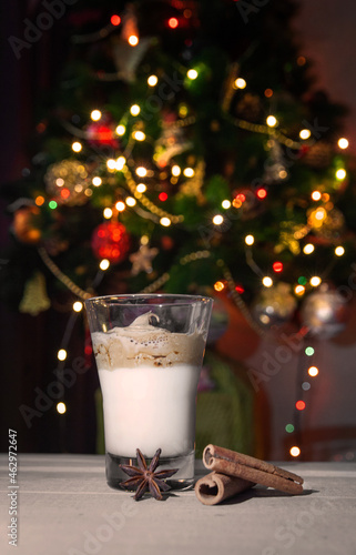Dalgona coffee in a transparent glass on a wooden table against the background of a Christmas tree. Selective focus.