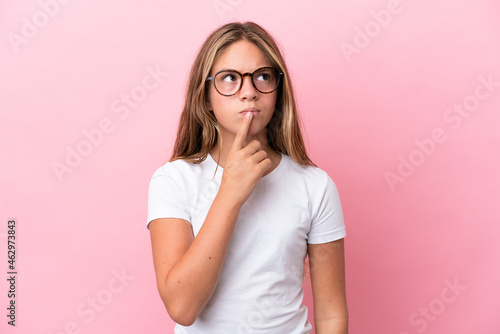 Little caucasian girl isolated on pink background With glasses and having doubts