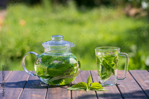 Healthy nettle tea in a glass tea pot and mug in the summer garden on wooden table