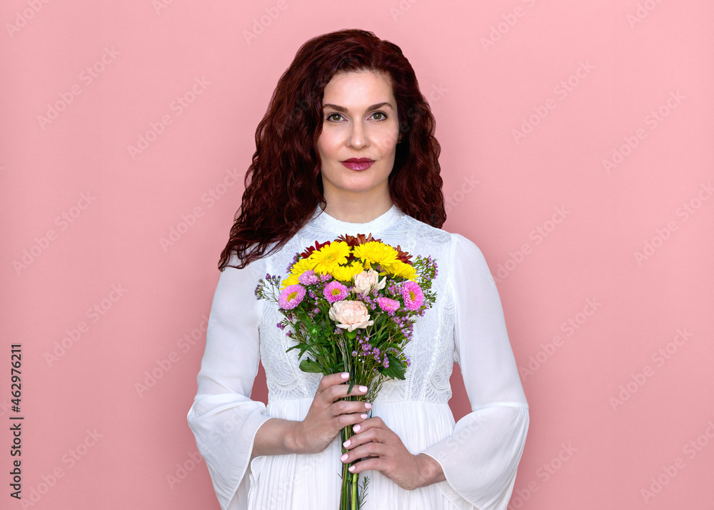 Woman Holding Flowers in Front of Her Chest with Pink Background. Romantic studio portrait of beautiful woman in white dress holding bouquet of colorful flowers. Woman Holding Flowers in Front of Her Chest with Pink Background. Romantic studio portrait of beautiful woman in white dress holding bouquet of colorful flowers.