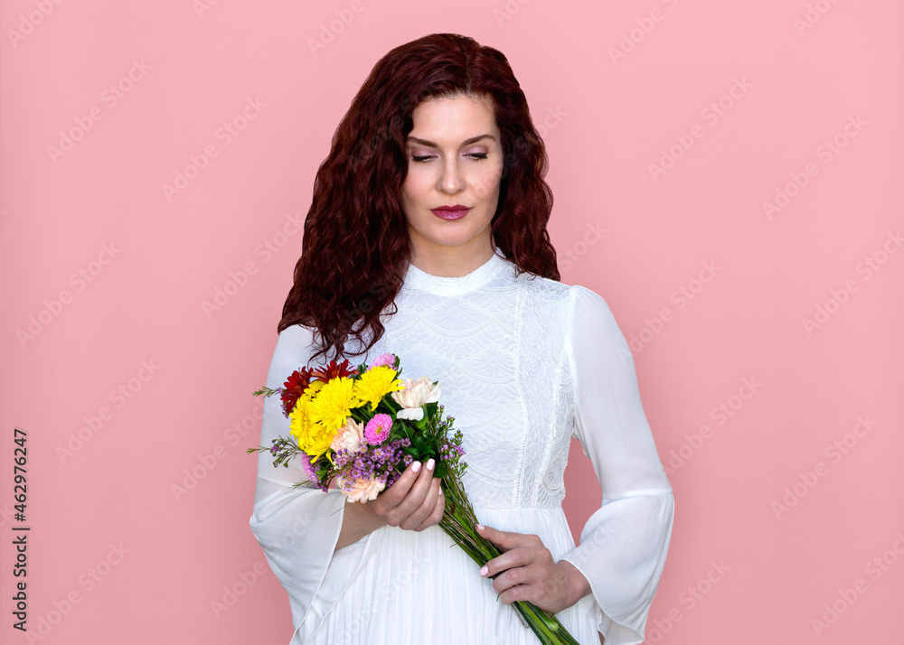 Woman Looking Down Holding Flower Bouquet with Pink Background. Beautiful pensive woman in romantic white dress holding bouquet of yellow and red Gerbera daisies, orange carnations, and purple mums. Woman Looking Down Holding Flower Bouquet with Pink Background. Beautiful pensive woman in romantic white dress holding bouquet of yellow and red Gerbera daisies, orange carnations, and purple mums.
