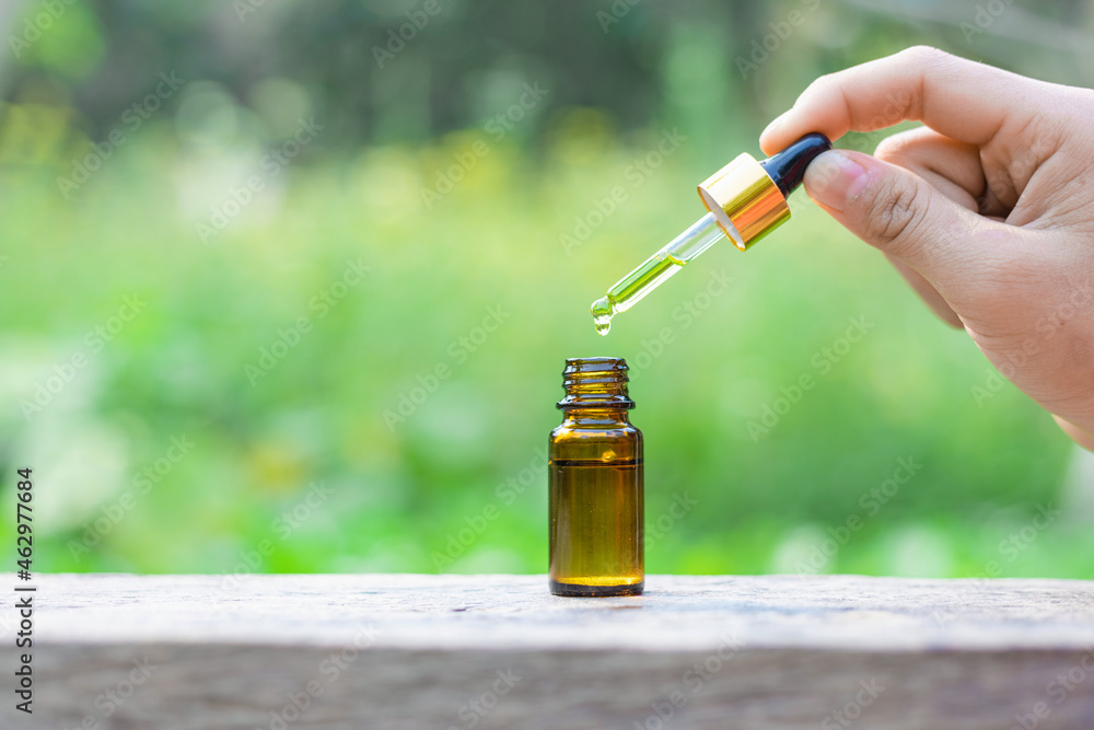 Hand holding essential oil falling from glass dropper. Bottle of cosmetic oil with a pipette on a wooden. Copy space. Selective focus. Hand holding essential oil falling from glass dropper. Bottle of cosmetic oil with a pipette on a wooden. Copy space. Selective focus.