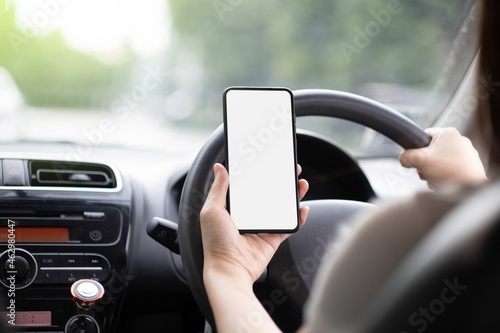 A woman driving a black car on a highway road. Hand holding a white touch screen mobile phone. Smartphone concept for text input and copy specs. © Thassanee