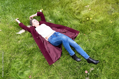 Young woman with afrokos lies in coat on green autumn grass . Wallow in the grass and enjoy life. Autumn mood. Freedom. photo