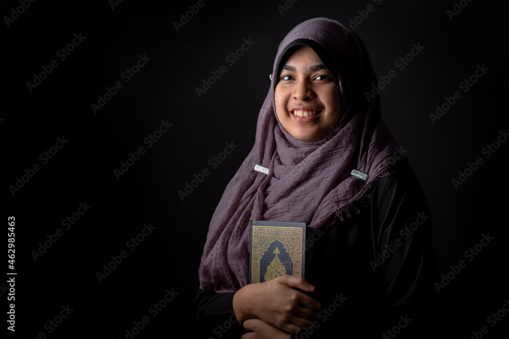 Portrait Asian Muslim woman standing and reading the Quran and appreciates and faith The Holy Al Quran with written Arabic calligraphy meaning of Al Quran, Arabic word translation: The Holy Al Quran. Portrait Asian Muslim woman standing and reading the Quran and appreciates and faith The Holy Al Quran with written Arabic calligraphy meaning of Al Quran, Arabic word translation: The Holy Al Quran.