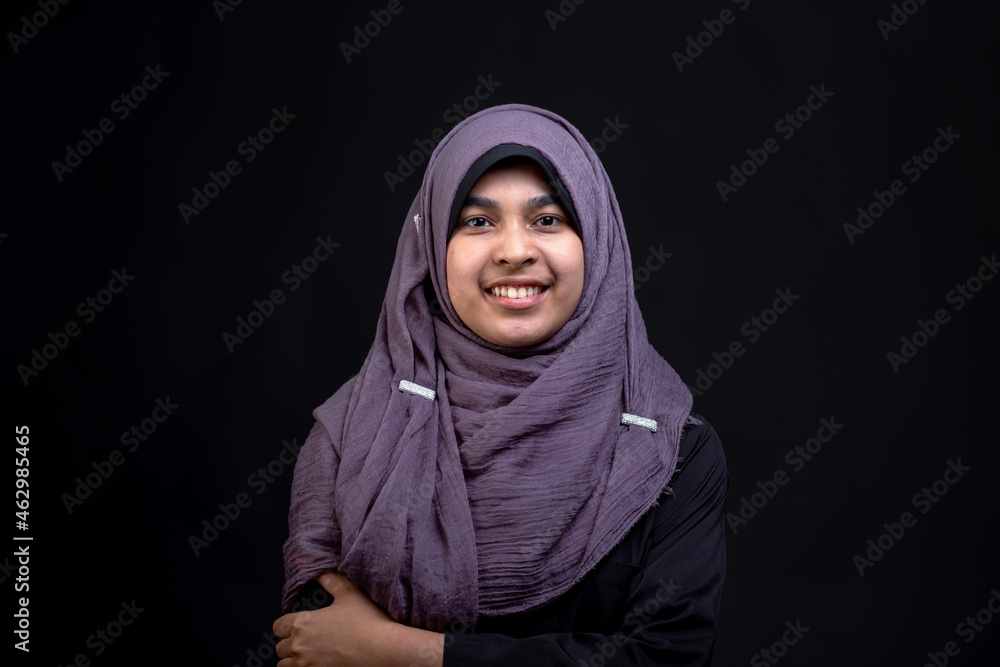 A beautiful Asian Muslim teenage girl is smiling, on an isolated black background, with copy space. A beautiful Asian Muslim teenage girl is smiling, on an isolated black background, with copy space.