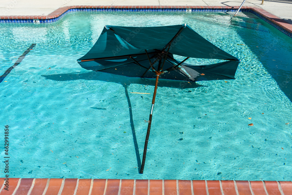 Broken large outdoor umbrella sitting at the bottom of the swimming pool after the storm. Torn