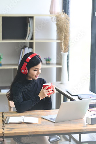 Smiling female listening to music in headphone and drinking coffee in office.