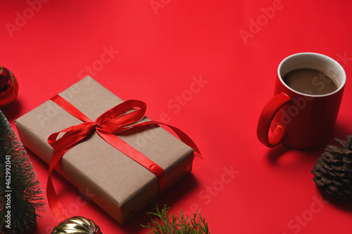 Fototapeta Naklejka Na Ścianę i Meble -  Christmas presents with red ribbon, pine cone, notebook and cup of coffee on red background.