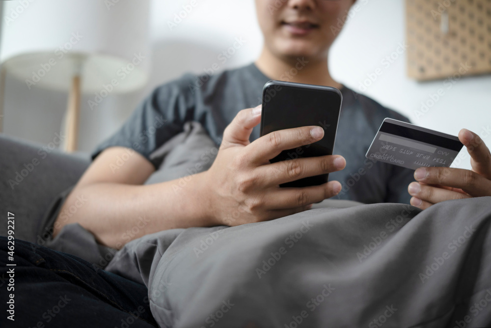 Cropped sot smiling young asian man shopping online on smart phone at home. Cropped sot smiling young asian man shopping online on smart phone at home.