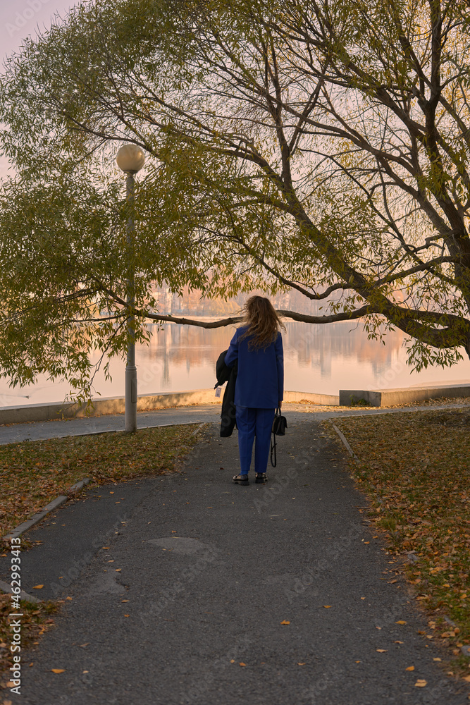 a young girl in an electric blue pantsuit walks alone after work in an autumn park in the afternoon in sunny weather