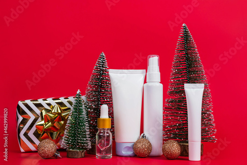 Fototapeta Naklejka Na Ścianę i Meble -  Copy space with night, day cream cosmetic oil, eye cream on red background with Christmas balls, trees. gift. Unbranded bottles in mockup style. Beauty background.