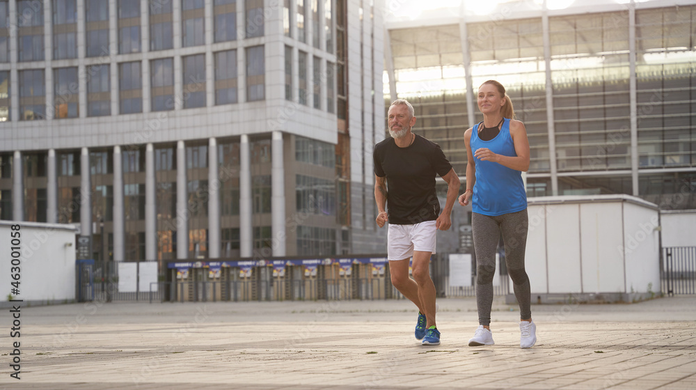 Sportive middle aged couple jogging together in the morning while training outdoors