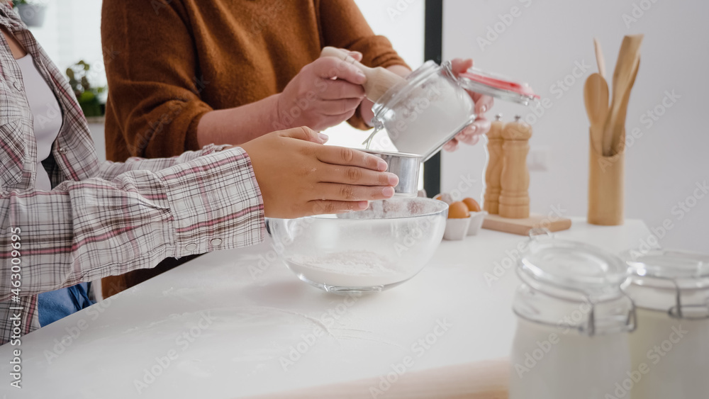 Closeup of grandmother hands putting flour in strainer while granddaughter sift ingredient in kitchen bowl preparing xmas homemade cookie dessert. Family celebrating christmas enjoying winter holiday Closeup of grandmother hands putting flour in strainer while granddaughter sift ingredient in kitchen bowl preparing xmas homemade cookie dessert. Family celebrating christmas enjoying winter holiday