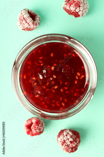 Jar of raspberry jam with ingredients on mint background