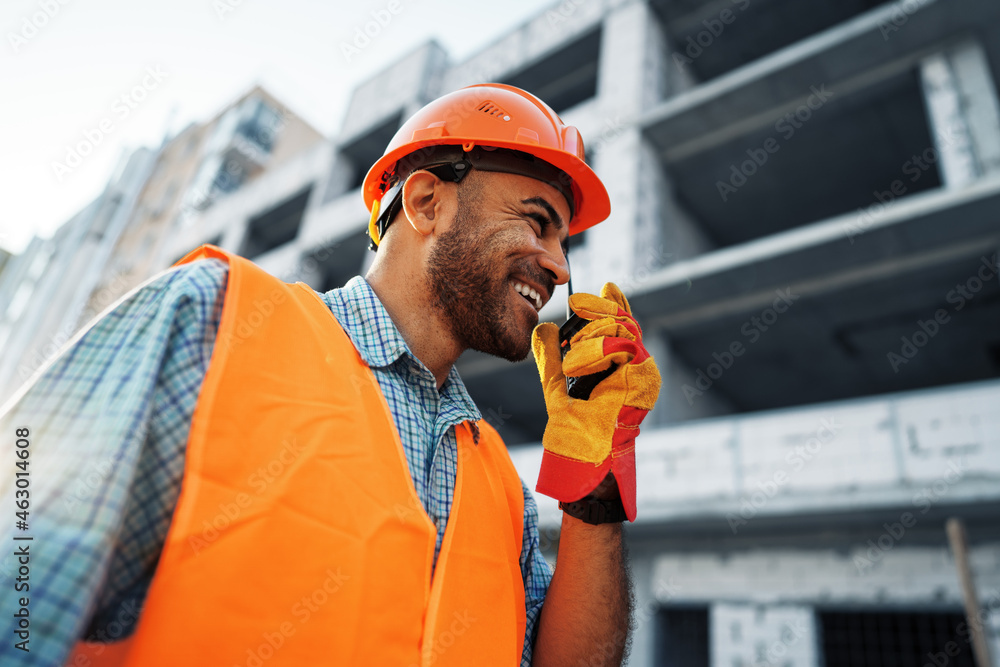 Young construction worker in uniform using walkie talkie on site - obrazy, fototapety, plakaty 