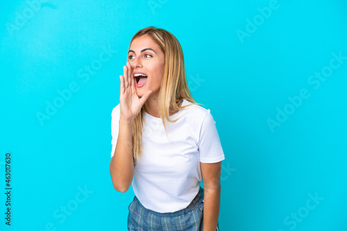 Blonde Uruguayan girl isolated on blue background shouting with mouth wide open to the side