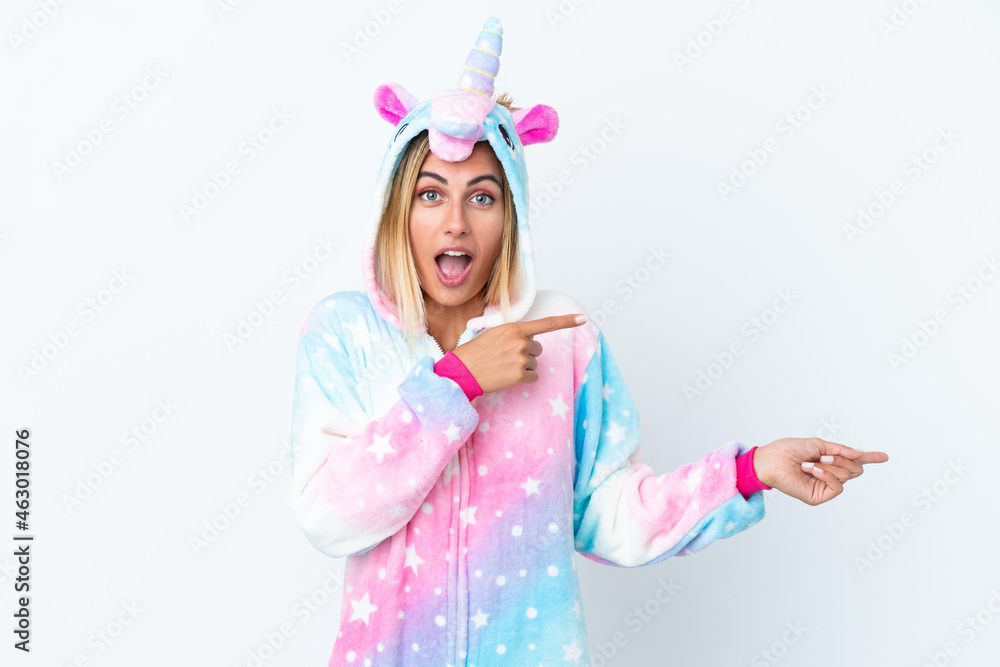 Blonde Uruguayan girl wearing a unicorn pajama isolated on white background surprised and pointing side Blonde Uruguayan girl wearing a unicorn pajama isolated on white background surprised and pointing side