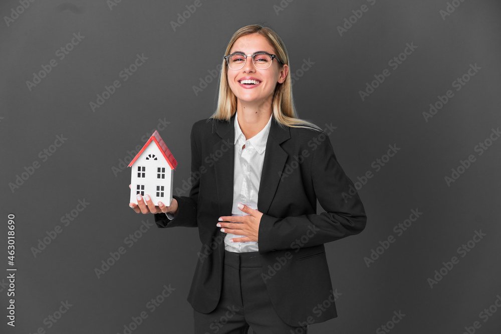 Blonde Uruguayan girl holding a house toy isolated on black background smiling a lot Blonde Uruguayan girl holding a house toy isolated on black background smiling a lot