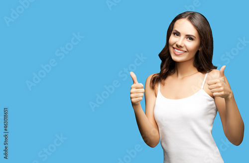 Photo of woman showing thumb up hand sign or like gesture, isolated on bright blue color background with mock up copy space. Portrait of happy smiling gesturing brunette girl at studio.