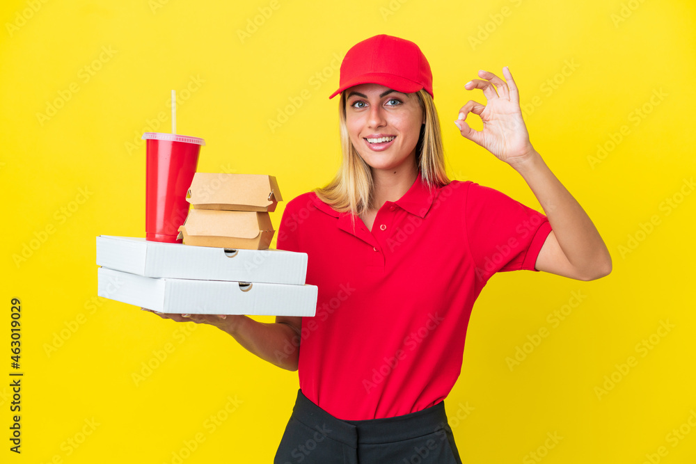 Delivery Uruguayan woman holding fast food isolated on yellow background showing ok sign with fingers Delivery Uruguayan woman holding fast food isolated on yellow background showing ok sign with fingers