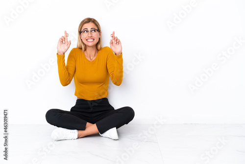 Blonde Uruguayan girl sitting on the floor with fingers crossing
